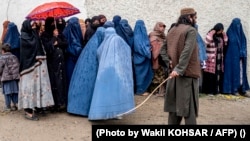 Cотрудник службы безопасности Талибана стоит на страже, пока афганские женщины в парандже стоят в очереди под проливным дождем, чтобы получить продукты питания, пожертвованные во время священного месяца Рамадан, Кабул, 25 марта 2025 года. Фото AFP
