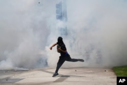 Протестующий бросает камень в струи слезоточивого газа, распыленные полицейскими во время протестов против антимигрантских рейдов, 7 июня 2025 года, Парамаунт, Калифорния, фото AP